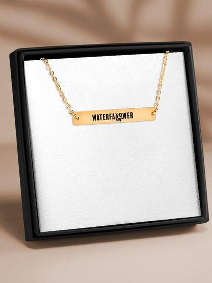 Gold necklace with 'WATERFALLFLOWER' pendant in a black box on a beige background