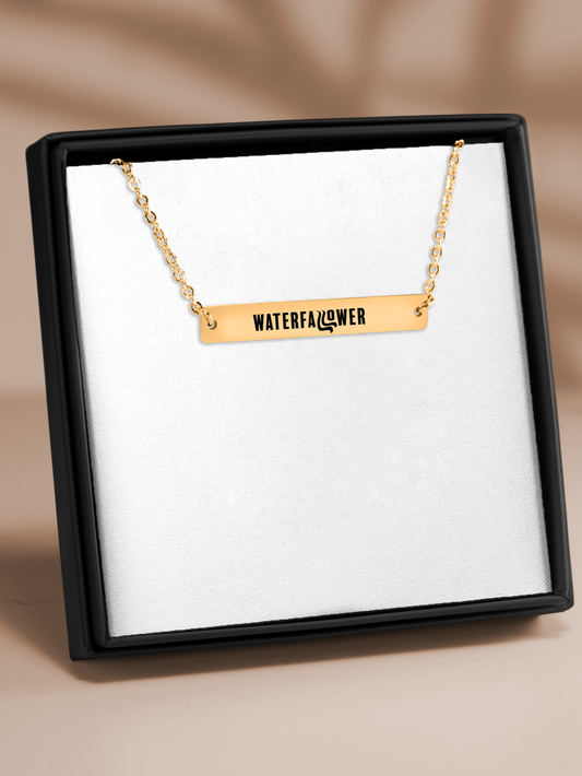 Gold necklace with 'WATERFALLFLOWER' pendant in a black box on a beige background
